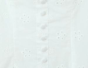 Detailed close-up of white floral embroidery and neat fabric-covered buttons on a dress