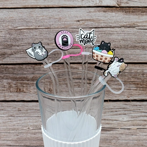 Detail of five cute cartoon cat silicone straw toppers on clear straws with wood background