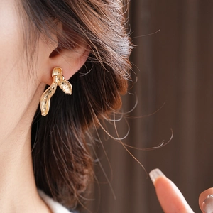 Detail view of a model wearing a gold pleated orchid petal earring with metallic texture