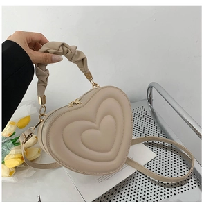 Close-up of heart-shaped quilted crossbody bag with ruffled handle and golden zippers