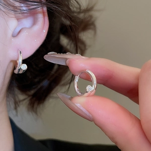 Détail de boucles d'oreilles créoles argentées avec pierre étoile portées par un modèle