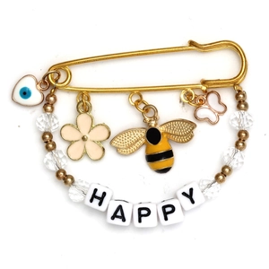Detailed close-up of golden safety pin brooch with HAPPY beads and evil eye charms