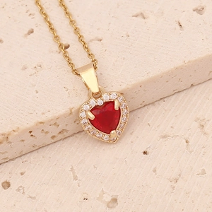 Close-up of gold heart necklace with a central red gemstone and zircon halo on stone