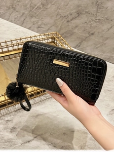 Detail of black crocodile texture wallet with gold metal bar and soft fur ball charm