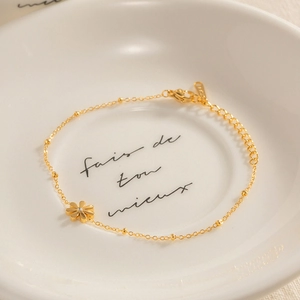 Detail of a gold daisy charm bracelet with sparkling rhinestone on white ceramic plate