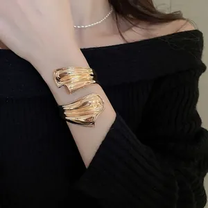 Unregelmäßiges goldenes Manschettenarmband mit welligem Flüssigkeitsdesign am Arm