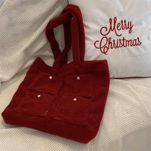 Close-up of a burgundy plush tote bag with colorful button pockets on a white knit blanket