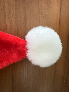 Detailed close-up of a plush red Christmas hat with a soft white pompom on wood