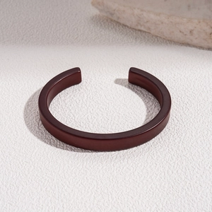 Close-up of matte dark brown acrylic geometric open cuff bracelet on textured stone