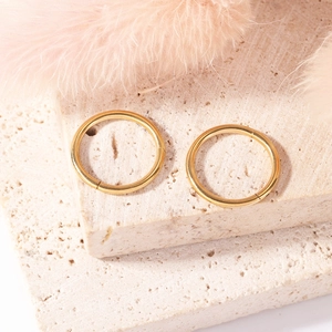 Polished gold stainless steel nose rings on marble background with soft feather accents