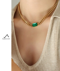 Detail of chunky gold Cuban chain necklace featuring a rectangular green emerald stone