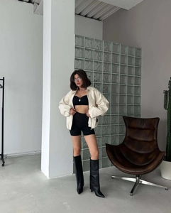 Women's white short zipper baseball jacket with black boots in an industrial studio