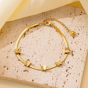 Detalle de una pulsera de serpiente dorada con dijes de mariposa sobre una base de piedra natural