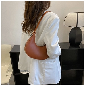 Brown leather crescent shoulder bag with silver hardware worn by a model in white suit