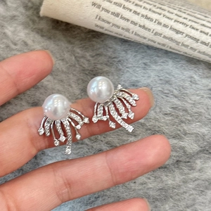 Macro detail of silver pearl earrings with radiant rhinestones held between fingers