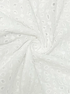 Détail macro du tissu brodé blanc avec motifs floraux et texture de coton doux