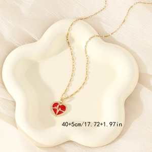 Gold heart pendant necklace with red enamel and crystals on a white ceramic plate