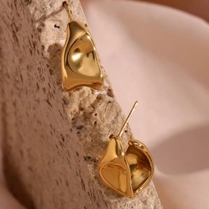 Macro shot of gold irregular fluid earrings on textured stone and soft cream fabric