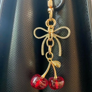 Detail of red cherry pendant with rhinestone bow charm hanging on a black leather bag