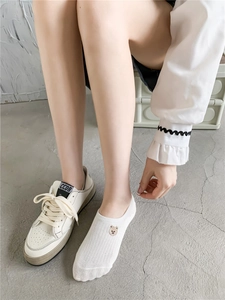 Close-up of white cotton invisible socks with bear embroidery and white sneakers