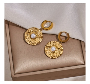 Macro detail of vintage gold pearl earrings with embossed texture on satin background