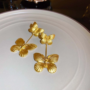 Detail of golden double-layer butterfly earrings with brushed metal texture on ceramic tray