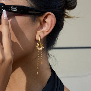 Détail des boucles d'oreilles à pompons lune et étoile dorées portées par un mannequin