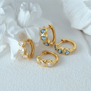 Detailed shot of golden huggie earrings with white and blue heart-shaped gemstones