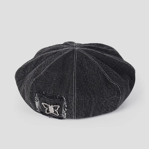 Detailed close-up of a denim beret featuring contrast stitching and silver butterfly patch