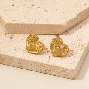Detailed view of gold heart stud earrings displayed on elegant beige stone blocks