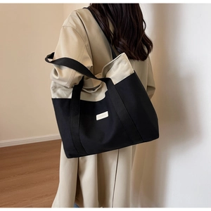 Close-up of a large canvas tote bag with black and beige contrast stitching and wide straps