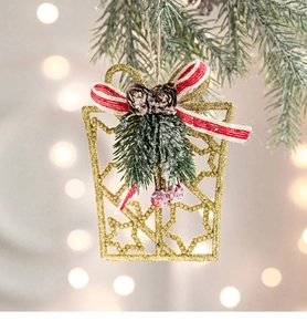 Golden glitter gift box ornament with red bow, pine cones and berries on Christmas tree