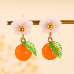 Detail of creative orange fruit earrings featuring white flowers and green leaves