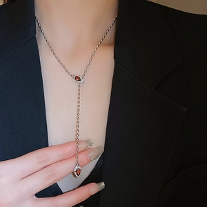 Detail of silver Y-shaped necklace with red teardrop stones worn on a black blazer