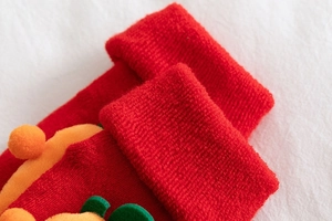 Macro detail of red festive knitted baby sock with green felt leaf and orange pompom