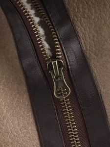 Detail of metal zipper and white plush lining on a vintage brown leather jacket