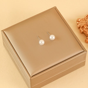 Elegant white pearl earrings with stainless steel pins on a golden jewelry box display