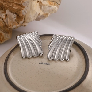 Macro shot of silver square earrings with a pleated wave texture on a ceramic base