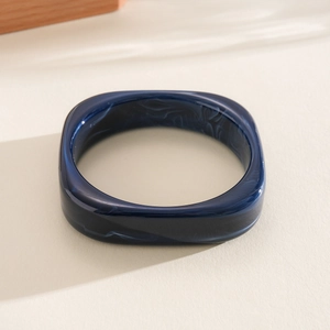 Detail view of dark blue resin bangle featuring white marble swirls and a square design.