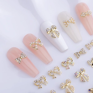 Detailed 3D golden bow nail charms with rhinestones and pearls on long manicured nails