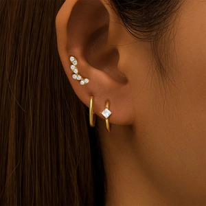 Detail of model wearing a gold ear cuff set with square zircon studs and hoop earring