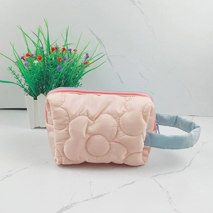 Detailed macro view of light pink quilted makeup bag with 3D flower pattern on marble