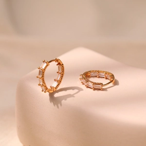 Macro shot of 18K gold huggie earrings with baguette-cut zircons on a stone display