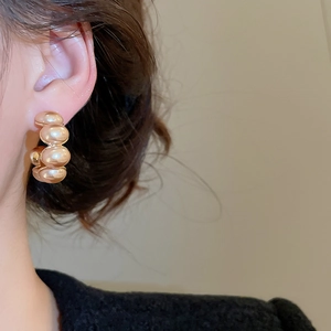 Close-up of gold-plated C-shaped bead earrings on a model with a polished shiny finish
