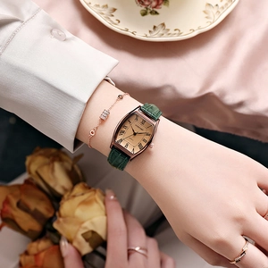 Gros plan d'une montre vintage carrée pour femme avec bracelet en cuir vert et bijou