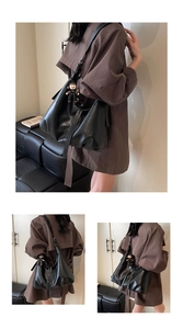 Detail of black leather hobo bag with adjustable strap and cute doll pendant on a model