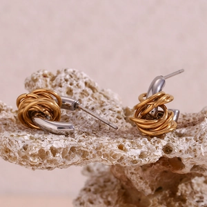 Close-up of two-tone twisted C-shape earrings in gold and steel on a natural stone