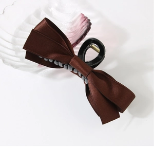 Detail of dark coffee satin bow hair claw clip showing glossy fabric and metal spring