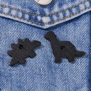 Minimalist black matte dinosaur pins on denim fabric with butterfly clutch backs