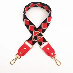 Detail of red and black jacquard woven bag strap with red leather ends and gold metal hooks